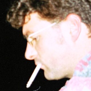 Two men, one climbing, the other smoking, in darkness.