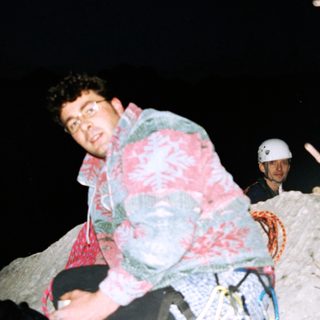 Two men rock climbing at night, wearing helmets and jackets.