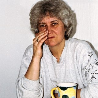 Here's a brief summary of the image: Older woman with short hair, touching her eye.