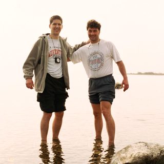 Two men standing in shallow water near a rock.