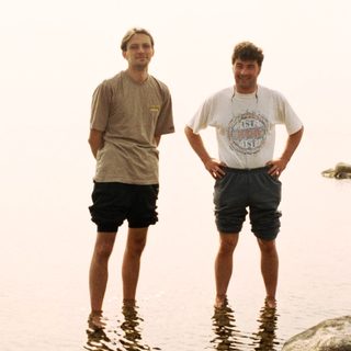 Two men stand in shallow water, looking at the camera.