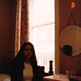 Woman sits near a window in a bedroom.