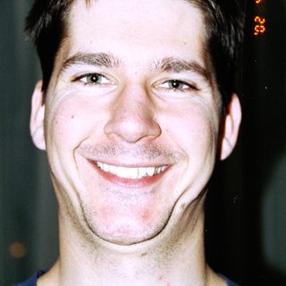 Here's a brief summary: Smiling man with short hair and a blue shirt.