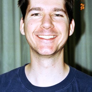 Here's a brief summary: Man smiling for a portrait, wearing a blue t-shirt.