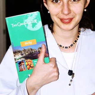 Woman holds up a "Green Guide" travel book about Sicily.