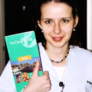 Woman holds up a "Green Guide" travel book about Sicily.