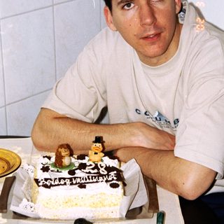 Man stands next to a birthday cake with decorations.