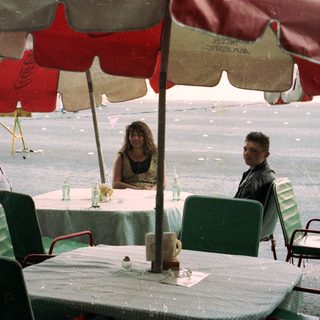 People seated at an outdoor table during rainfall.