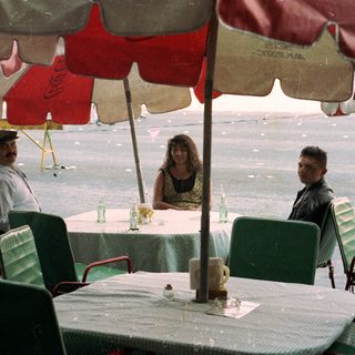 People seated at an outdoor table during rainfall.