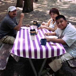 Family sits at a picnic table in a wooded area.