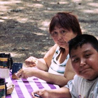 Family sits at a picnic table in a wooded area.