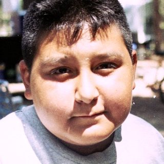 Boy wearing a Lakers shirt sits at a picnic table.