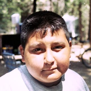 Boy wearing a Lakers shirt sits at a picnic table.
