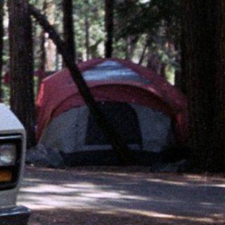 Man stands near a vintage camper van in a campsite.