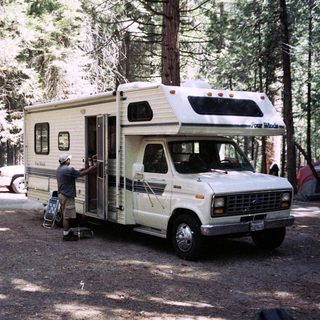 Man stands near a vintage camper van in a campsite.