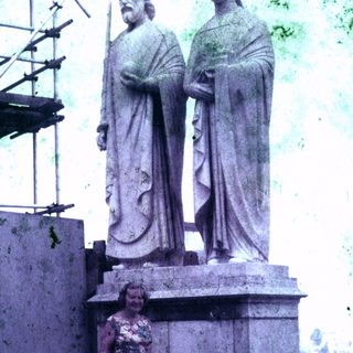 Woman stands near a large, ornate statue outdoors.