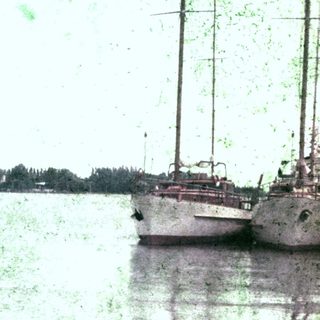 Woman sits by a lake, near boats and trees.