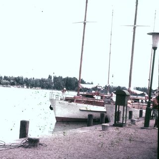 Person stands near a boat on a waterfront dock.