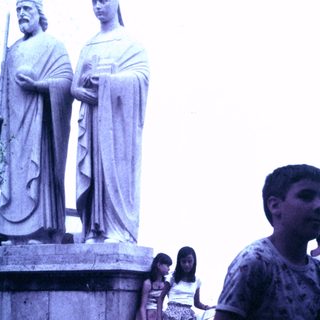 Here's a brief summary of the image: Boys and girls stand near a large, classical statue.