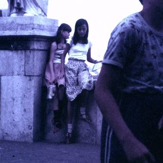 Here's a brief summary of the image: Boys and girls stand near a large, classical statue.