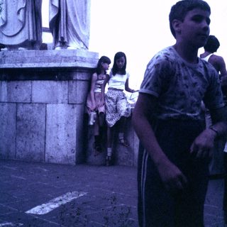 Here's a brief summary of the image: Boys and girls stand near a large, classical statue.