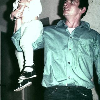 Man carrying a child indoors, possibly a father and daughter.