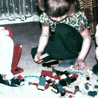 Two young girls playing with building blocks on a carpet.