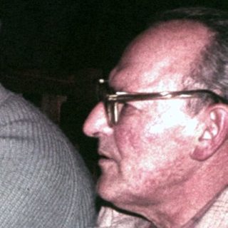 Men sit at a table with drinks, appearing to converse.