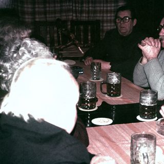 Men sit at a table with drinks, appearing to converse.
