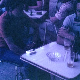 Men seated at a table outdoors, appearing to socialize.