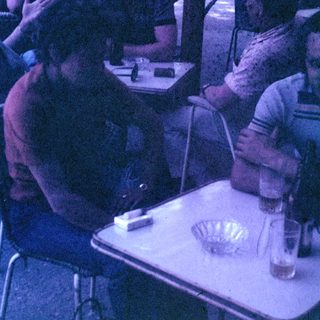 Men seated at a table outdoors, appearing to socialize.