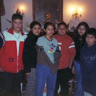 Here's a brief summary of the image: Group of young people posing indoors, likely family or friends.