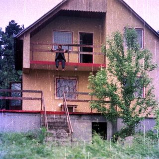 Here's a brief summary of the image: Person hanging from a balcony of a multi-story building.