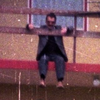 Here's a brief summary of the image: Person hanging from a balcony of a multi-story building.