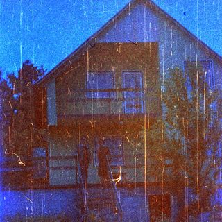 Blue toned image shows a house with a balcony.