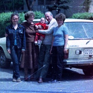 Family stands near a car in front of a building.