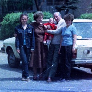 Family stands near a car in front of a building.