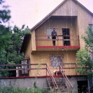 A man stands on a balcony of a two-story house.
