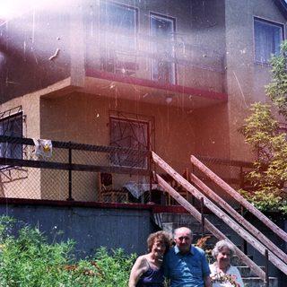 Three people stand in front of a building with a balcony.