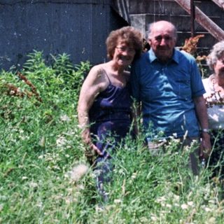 Three people stand in front of a building with a balcony.