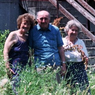 Three people stand in front of a building with a balcony.