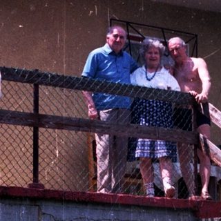 Here's a brief summary of the image: Two people on a balcony overlooking overgrown vegetation and stairs.
