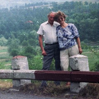 Couple standing on roadside overlooking forested, hilly landscape.