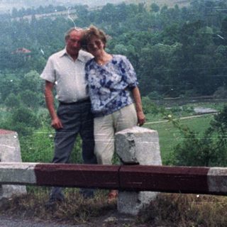 Couple standing on roadside overlooking forested, hilly landscape.
