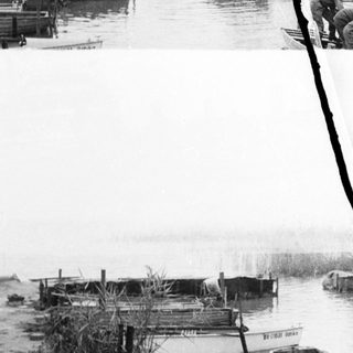 Here's a brief summary of the image: Men work on boats near a riverbank.