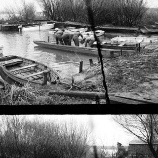 Men inspecting and working on boats near a riverbank.