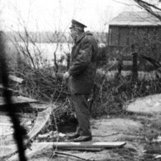 Men inspecting and working on boats near a riverbank.
