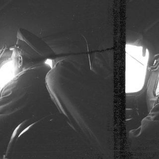 Here's a brief summary of the image: Man in uniform looking out of an aircraft window.