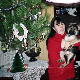 Woman holding a puppy near a Christmas tree.