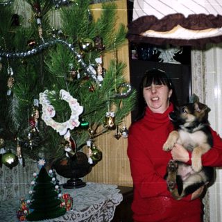 Woman holds a puppy near a decorated Christmas tree.